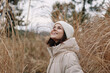 © SHOTPRIME STUDIO - Woman outdoors smiling in a light jacket among tall grass, enjoying a crisp day. A candid portrait in nature with soft earth tones, a calm mood and tranquil scenery.