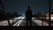 © GMeta - Silhouette on a night bridge above railway tracks as long-exposure light trails streak below