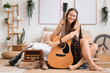 © Pixel-Shot - Young happy female hippie with peace symbol, vintage radio receiver, books and guitar sitting on floor in bedroom