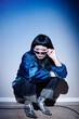 © Seventyfour - Asian young adult woman crouching near wall, holding sunglasses and looking directly at camera, wearing metallic boots, embodying second hand fashion style in urban setting