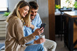 © NDABCREATIVITY - Happy couple relaxing at home with coffee, enjoying online shopping and shared digital experiences