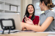 © bongkarn - Smiling asian woman talking to a coworker as sitting with working material on table in office studio