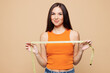 © ViDi Studio - Young smiling happy woman wear orange casual clothes hold in hand measure tape show result isolated on plain pastel light beige background. Proper nutrition healthy fast food unhealthy choice concept.