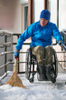 © Alex - A wheelchair user in a blue jacket sweeps his ramp with a broom