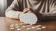 © Artfinity - Mental health awareness and cognitive brain function. Neurology research and memory puzzle solution. Person sitting at a table with a brain shaped puzzle and scattered pieces
