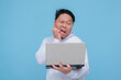 © Hatriansyah - Young Asian man showing shocked expression when seeing his laptop error wearing white t-shirt on turquoise blue background