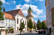 © Agnieszka Gaul - Visitors and locals alike enjoy a sunny day in Bratislava's historic Main Square (Hlavné námestie), which is anchored by the iconic yellow Old Town Hall tower and the white Jesuit Church.