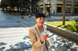 © Marko Geber - Smiling businesswoman using smartphone on city street