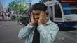© Krakenimages.com - Hispanic man in light denim shirt holds face with both hands on bustling urban street in daylight; surprise.