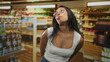 © Krakenimages.com - Young woman with glasses sticks tongue out and tilts head in supermarket aisle wearing white tanktop and jeans; playful spontaneity.