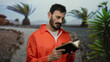 © Krakenimages.com - Hispanic man with beard in orange jumpsuit holds bible in outdoor park setting surrounded by green trees and reflects on faith while standing in nature.