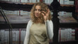 © Krakenimages.com - Woman with curly hair wearing beige apron making ok sign with right hand in studio library set beside bookshelves and ladder; approval.