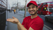 © Krakenimages.com - Man in red courier uniform with open palms presenting on bustling city street near double decker bus; friendly service.