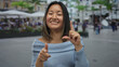 © Krakenimages.com - Young woman pointing at camera while smiling on city terrace with bustling restaurant and street backdrop creating a lively outdoor urban scene.