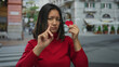 © Krakenimages.com - Young woman in red holds paper heart on city street, gestures no with finger, displaying disapproval.