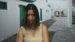© Krakenimages.com - Woman expressing discontent in urban street setting with white buildings and green doors on a sunny day outdoors, wearing casual top, surrounded by architectural details.