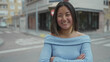 © Krakenimages.com - Young chinese woman in a blue sweater stands confidently on a quiet city street with crossed arms, capturing the essence of urban outdoor life.