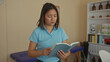 © Krakenimages.com - Woman reading book in clinic room, surrounded by medical equipment and shelves, suggesting a healthcare setting featuring a young professional in china.