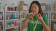 © Krakenimages.com - Woman talking on phone in donation center wearing green volunteer t-shirt surrounded by shelves and boxes indoors