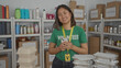 © Krakenimages.com - Woman volunteer wearing green shirt uses phone inside donations center surrounded by boxes and supplies indicating organization and communication.