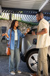 © wavebreak3 - African American friends exchanging coffee cups while charging electric vehicle under metal carport