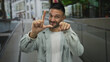 © Krakenimages.com - Young hispanic man making loser gesture while smiling at the camera in an urban street setting, showcasing a confident and playful demeanor outdoors.