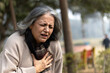 © Pix4Ads - Indian senior woman holding chest with pained expression sitting on bench outdoors. Possible heart diseases problem, outdoor got troubles with her chest pain or breathing difficulty in park