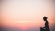 © Yuliia - Young woman meditating in lotus pose during sunset with peaceful pink sky background for wellness and mindfulness practices.