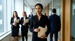 © Yuliia - Professional African American businesswoman walking confidently in modern office corridor holding documents with diverse colleagues in background.