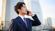© Yka - 夕暮れのビル街で電話連絡をする男性