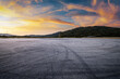 © zhao dongfang - Dramatic empty asphalt ground with tire marks near a green mountain under a beautiful sunset sky.