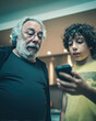 © Kowit - A grandfather and grandson share a moment, both captivated by a smartphone, highlighting the bond across generations.