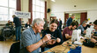 © Justice - Community members gather at a repair cafe, fixing various items together at a table, focused on sustainability and social connection.