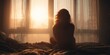 © vetrana - Sad woman sits on bed looking out window at sunrise in a quiet room with soft light