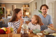 © Stockphotodirectors - A family shares a joyful breakfast in their warm kitchen, with a mother feeding her child and a father serving food. Laughter fills the air as they connect during this special time.