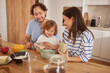 © Stockphotodirectors - A cheerful family is gathered around the kitchen table preparing breakfast. Parents and child are smiling, enjoying each other's company and sharing food.