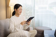 © matinee - Young woman relaxing on a sofa at home while using a digital tablet. Cozy indoor lifestyle and modern technology concept.