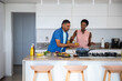 © wavebreak3 - Couple preparing burgers on kitchen island with sliced vegetables, sauce bowl and condiment bottles