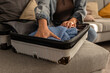 © blackday - Woman pressing down folded sweater inside open suitcase, efficient packing at home