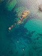© AmazingAerialAgency - Aerial view of a rocky island surrounded by turquoise waters, with two kayakers paddling nearby, Crozon, Finistre, France.