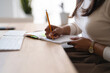 © Studio Marmellata - A person is writing in a notebook with a pencil at a desk with a keyboard and a plant in the background.