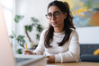© Studio Marmellata - A woman wearing glasses is focused on her laptop, taking notes with a pencil. She is working at a desk in a bright, modern room.