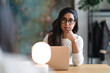 © Studio Marmellata - A woman wearing glasses sits at a desk with a laptop and a lamp, deep in thought as she works.