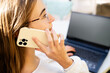 © Соня Монштейн - Close up of a young business woman talking on the phone and working on a laptop in the office, view from behind