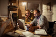 © Davor - Smiling couple collaborating on laptop at night in home office