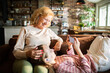 © Geber86 - Grandmother and granddaughter with hearing aids watching smartphone on sofa at home