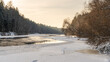 © Edijs - Winter river bend at golden dusk with snow covered banks and forest reflections, serene northern landscape evoking warmth, stillness and quiet seasonal harmony