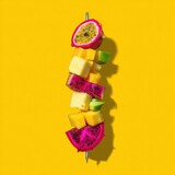 A vibrant skewer features exotic fruit against a bright yellow background