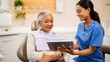 © SerPak - A dentist in blue scrubs shows a senior patient information on a tablet during a dental consultation. Modern dental care experience.