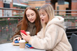 © Iryna - Two friends sit at a table looking at a phone in a cafe on a sunny day in the city